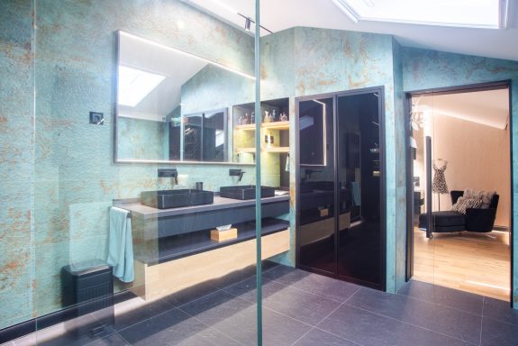 Baño moderno con paredes verdes, espejos grandes y gran mampara de cristal de seguridad. Suelo de baldosas porcelánicas antideslizantes.