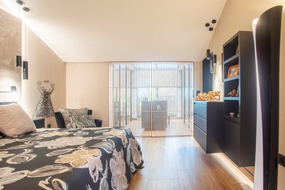Habitación moderna con cama, estantería negra y luz natural.
