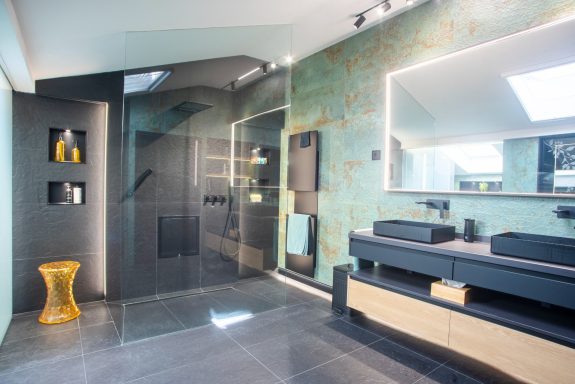 Baño moderno con paredes verdes, ducha de vidrio y mobiliario minimalista en tonos oscuros.
